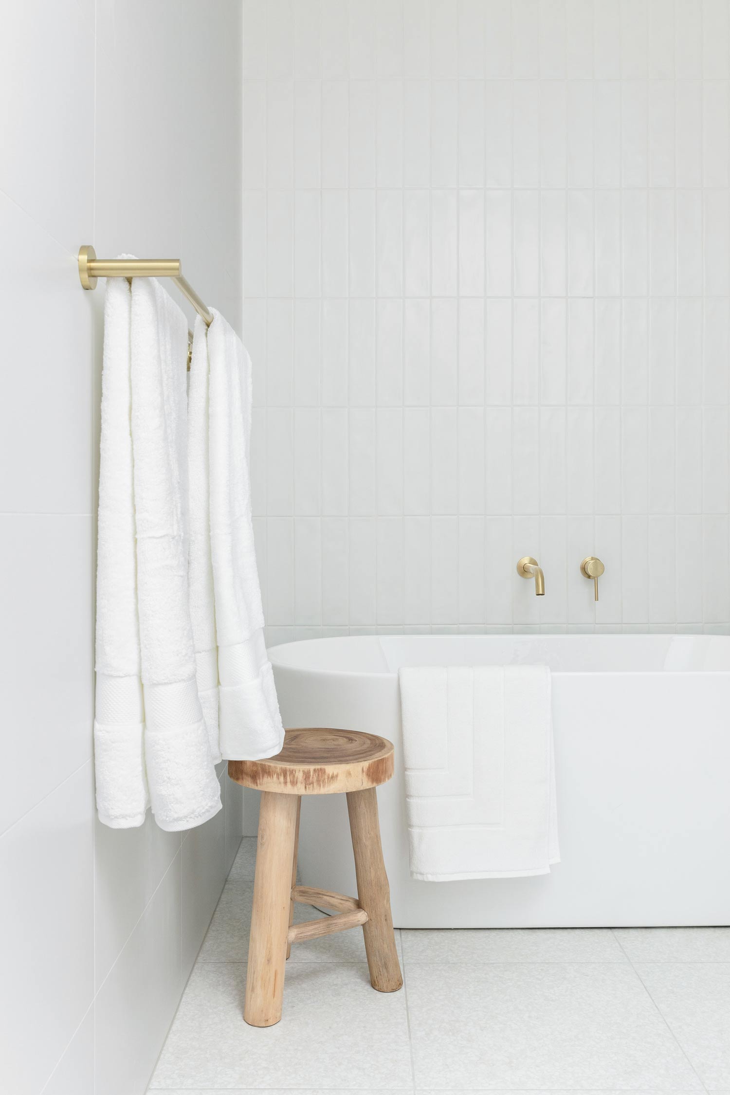 Modern-coastal-bathroom-featuring-brushed-brass-tapware-neutral-floor-tiles-and-white-vertical-tiles-with-timber-stool