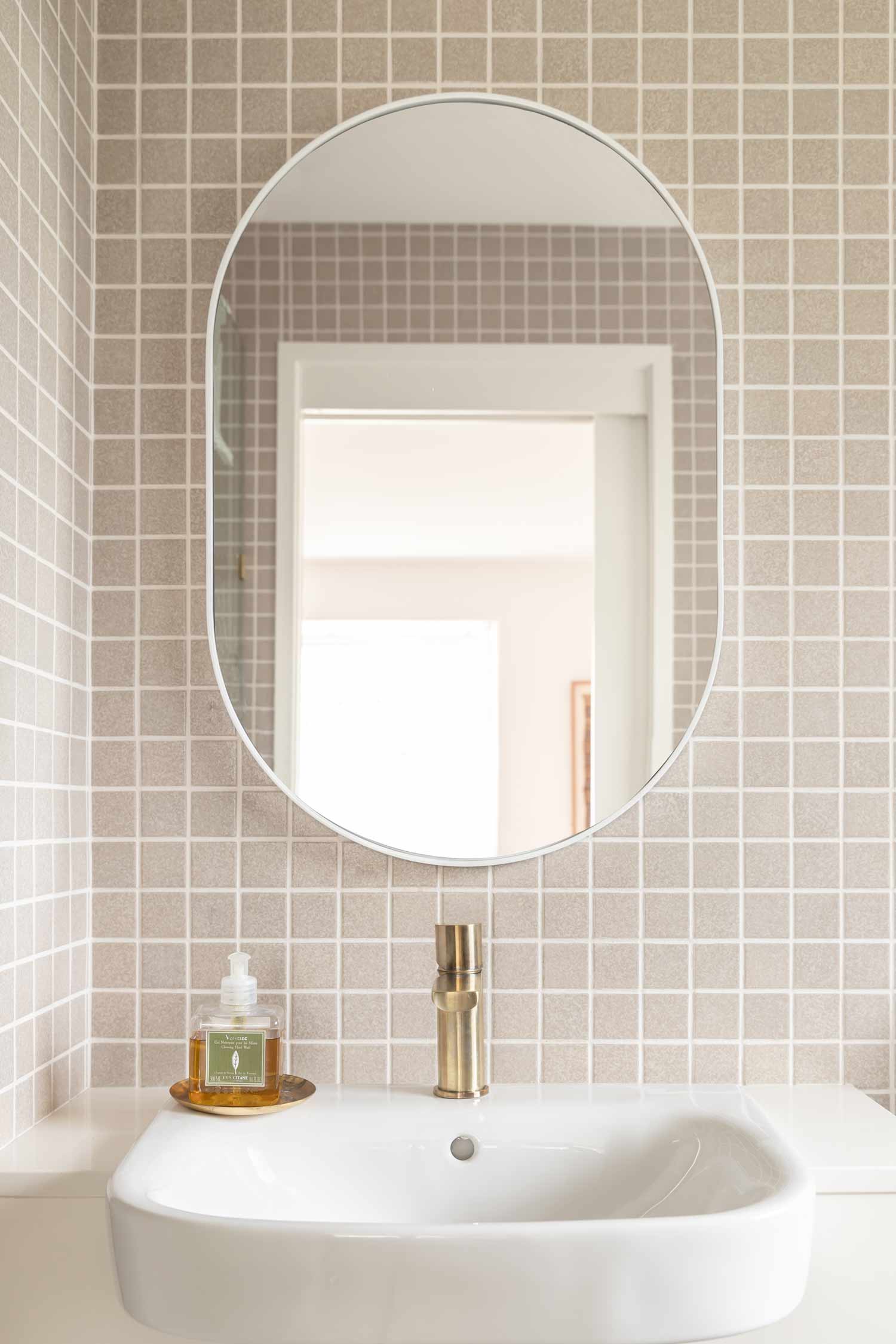 Japanese-mosaic-tiles-in-a-modern-coastal-bathroom-featuring-an-oval-mirror-and-brushed-brass-basin-mixer