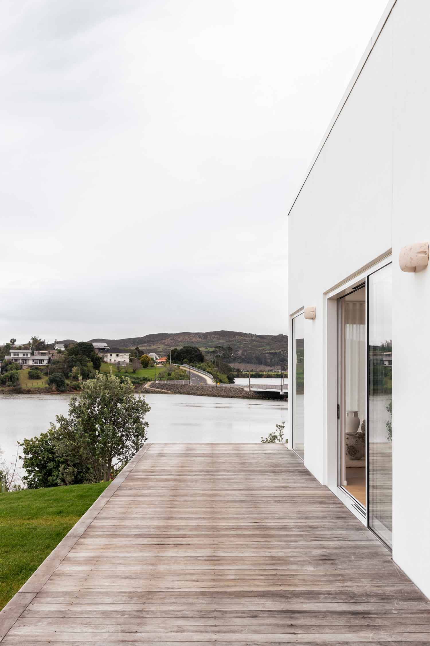 Exterior-of-a-moditerranean-home-with-timber-deck-and-white-exterior-paint-looking-out-to-a-lake
