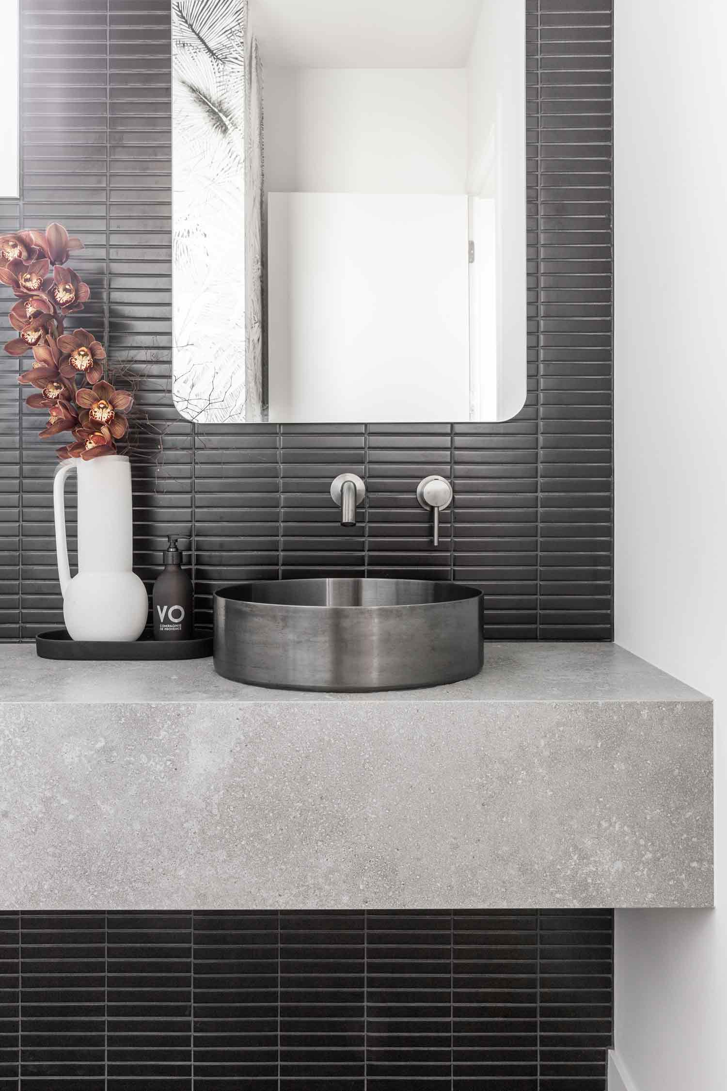 Dark-interior-design-in-a-contempory-house-features-black-kit-kat-tiles-a-stone-slab-vanity-and-gunmetal-sink-and-tapware