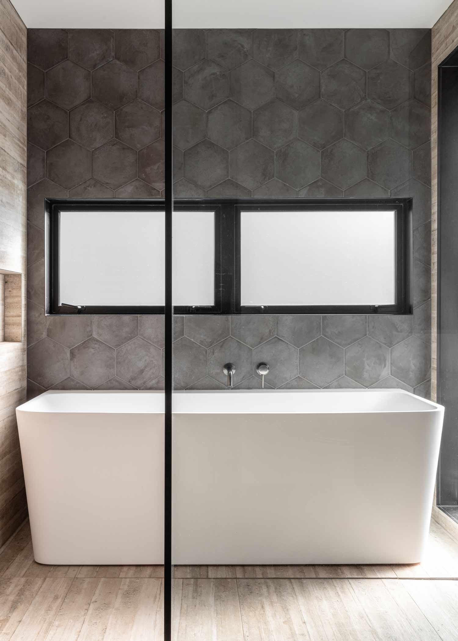 Timber-look-floor-tiles-and-dark-grey-feature-hexagonal-tiles-surround-a-bath-in-this-modern-industrial-bathroom