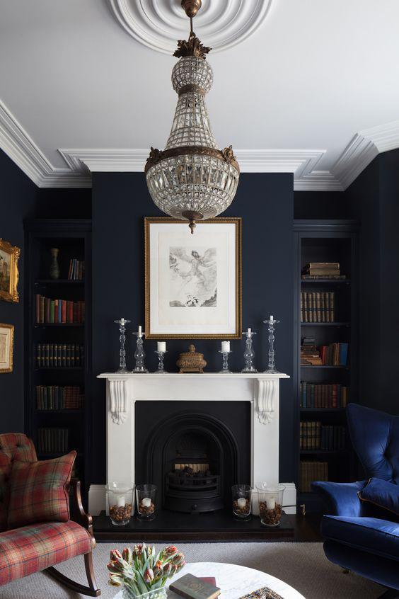A-crystal-chandelier-hangs-from-a-celing-rose-in-an-old-money-aesthetic-sitting-room-with-a-fire-place-and-tartan-and-velvet-arm-chairs