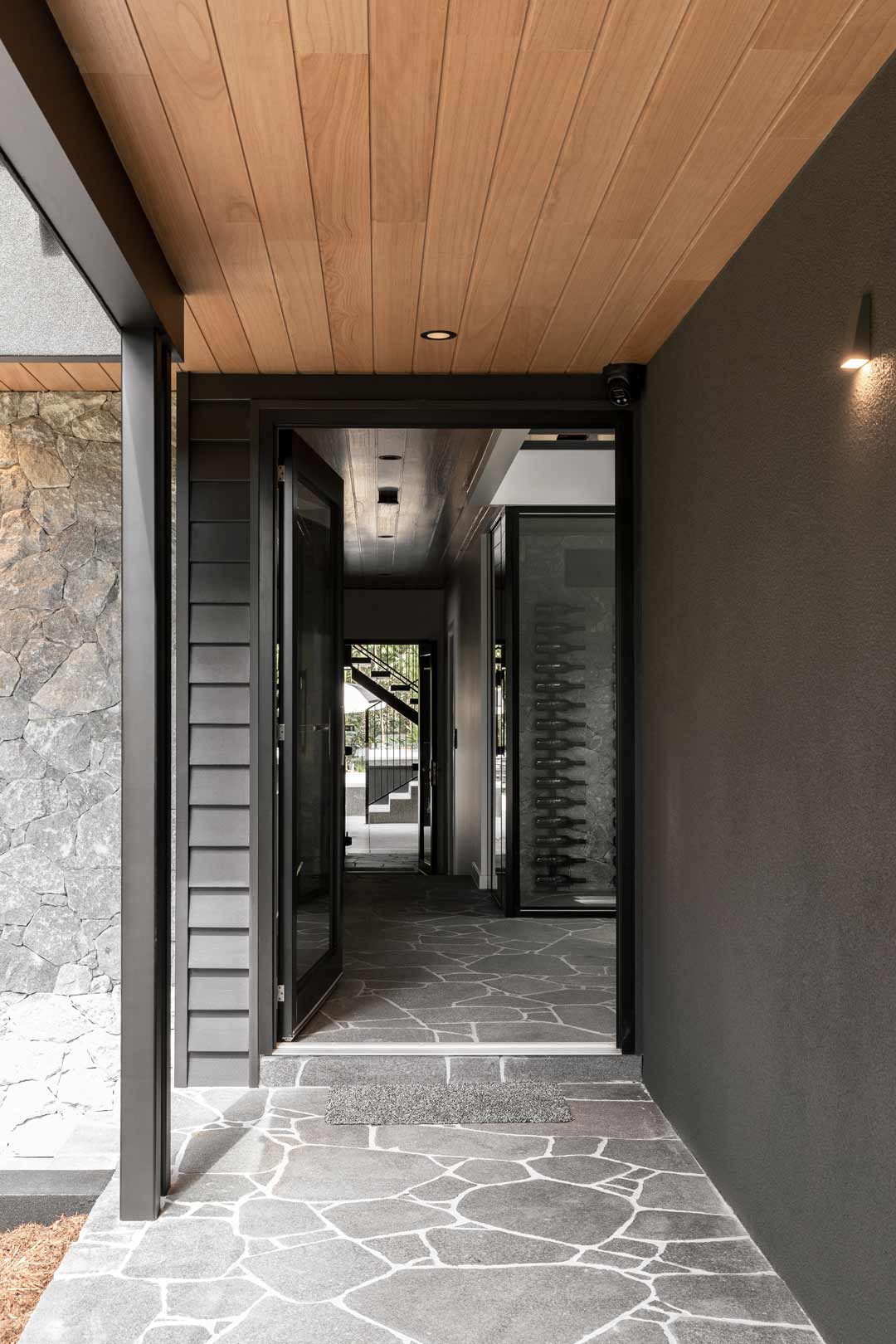 A-monochomatic-entryway-with-a-stone-feature-wall-and-path-a-timber-ceiling-and-wine-cellar-in-an-alpine-lodge-style-home