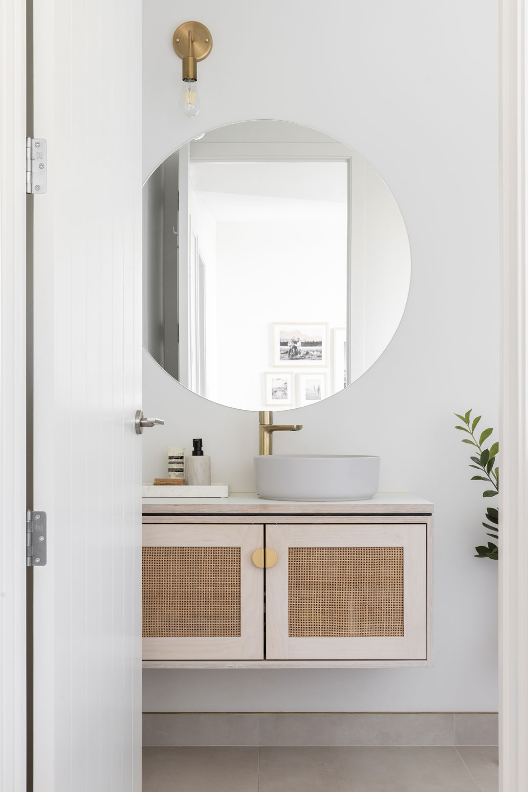 A-soft-coastal-bathroom-with-brushed-brass-tapware-a-rattan-vanity-and-round-mirror-and-basin