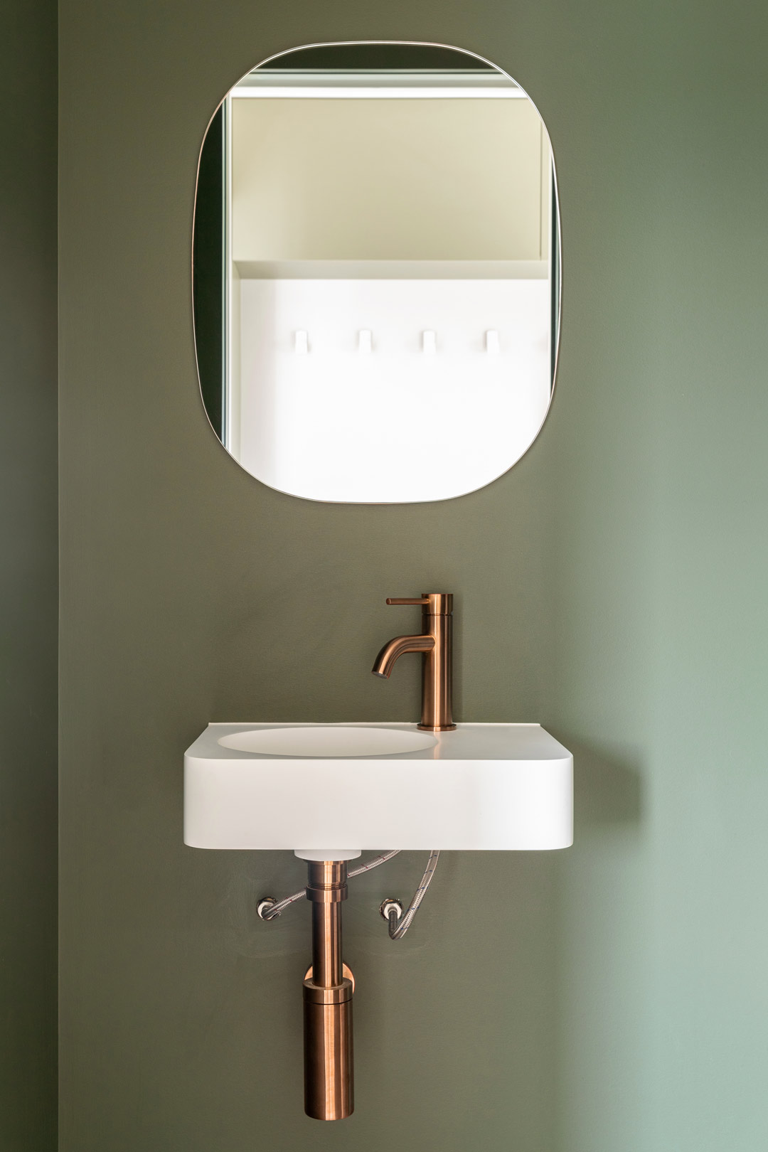 A-muted-green-powder-room-with-a-small-wall-hung-basin-and-brushed-copper-tapware