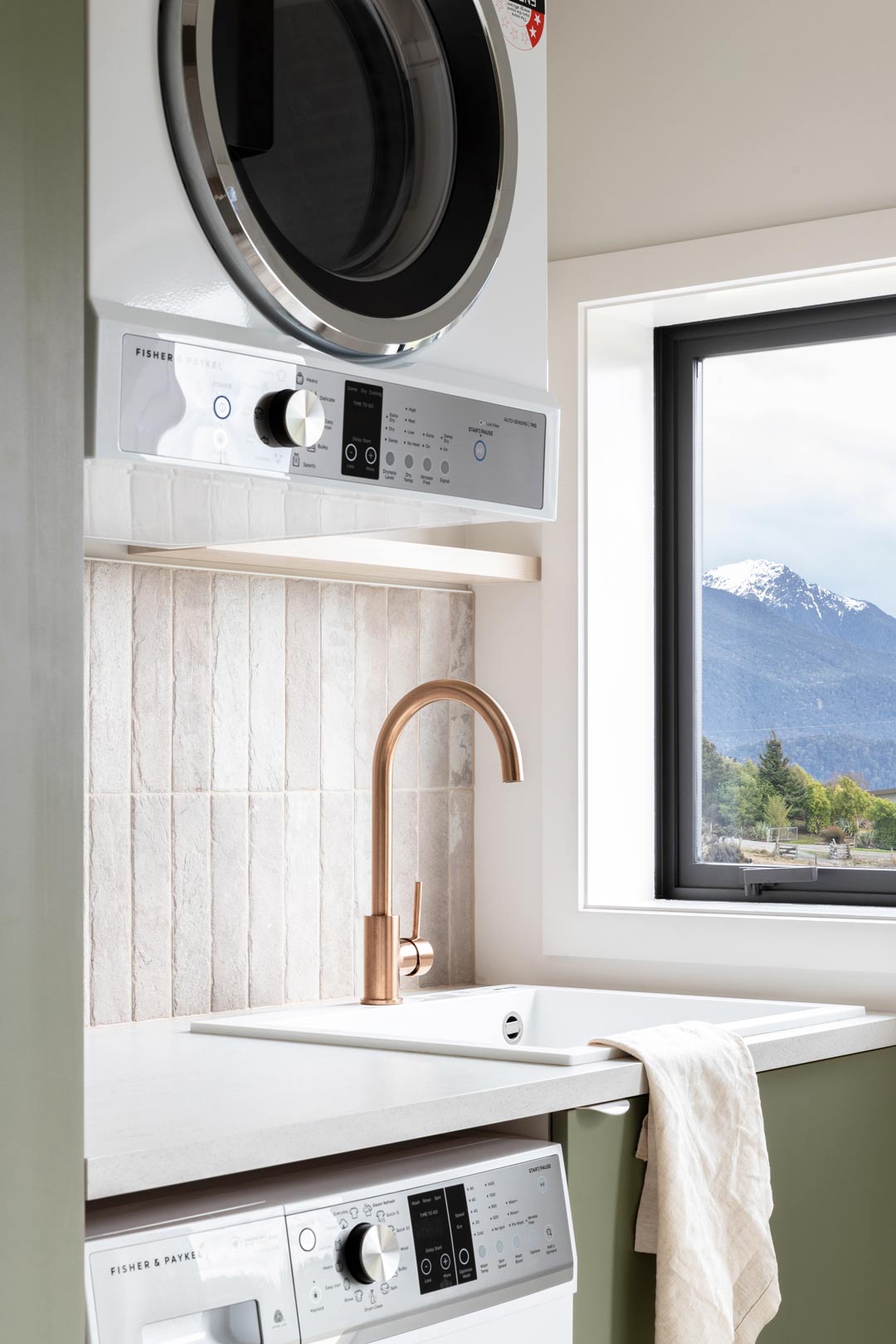 A-simple-laundry-with-mountain-views-neutral-subway-tiles-copper-tapware-and-green-cabinetry