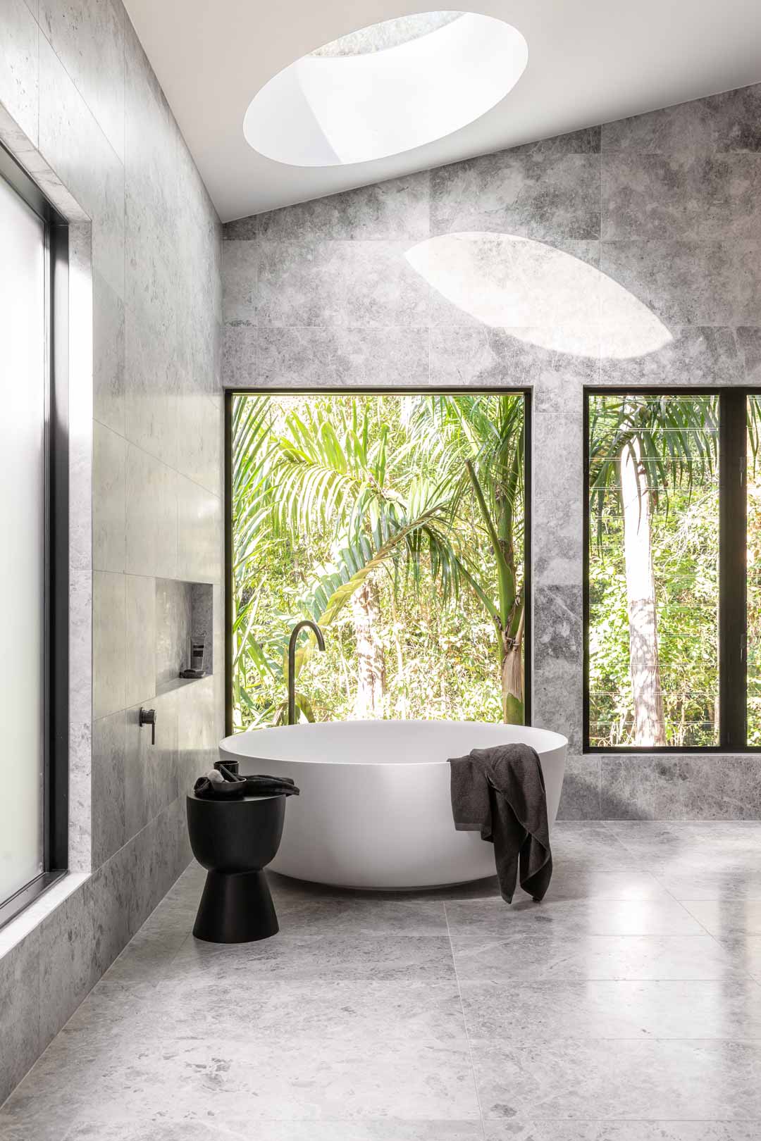 2.-Monochromatic-ensuite-bathroom-for-Kooringal-Lodge-with-circular-bath-skylight-and-windows-letting-the-outdoors-in