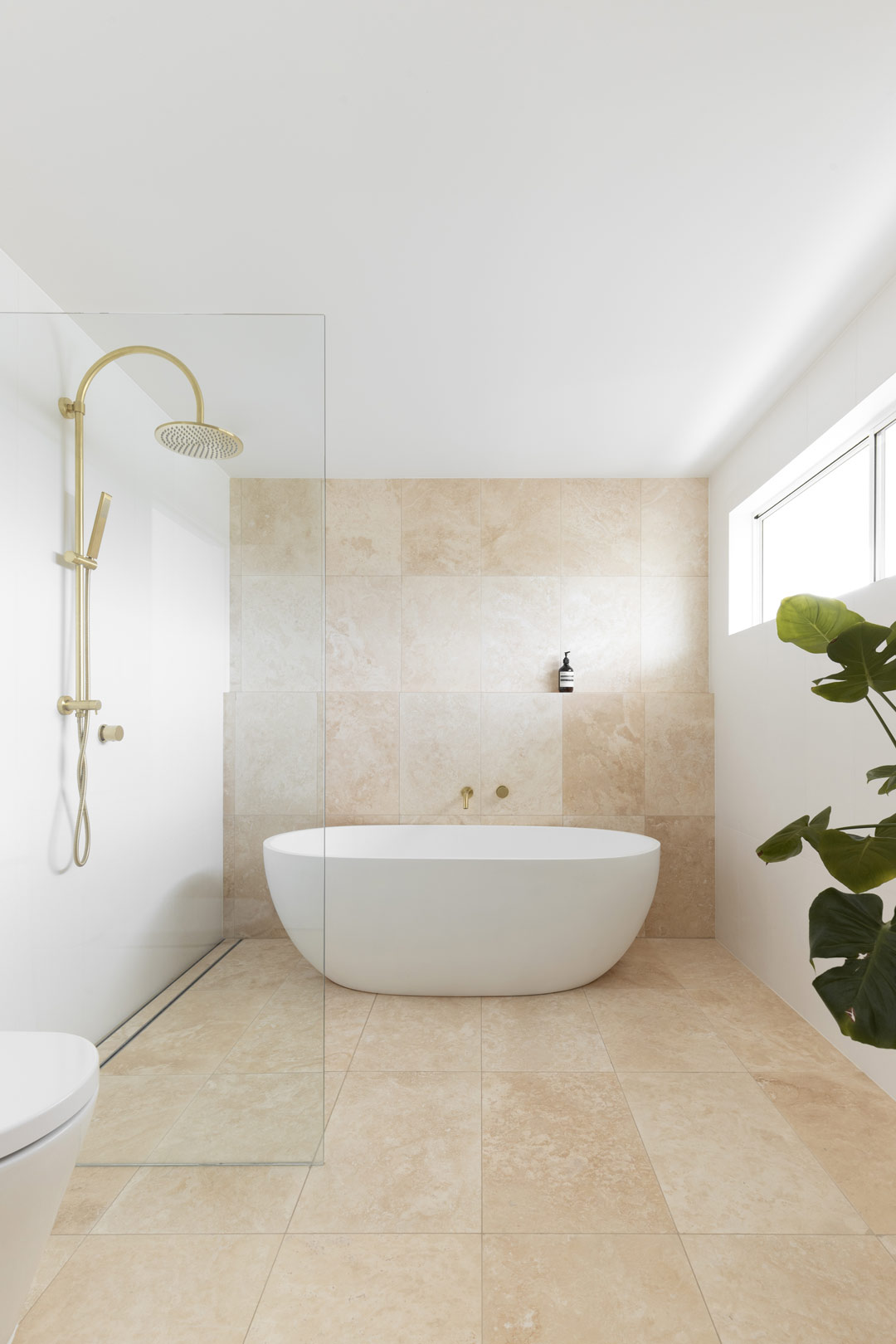 6.-A-freestanding-bath-in-an-open-wetroom-style-bathroom-with-brushed-brass-tapware-and-travertine-tiles