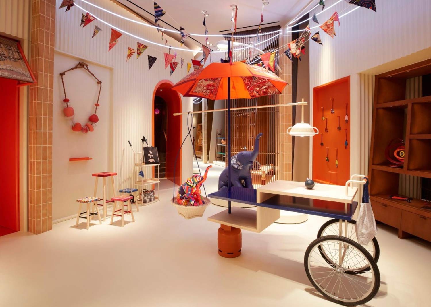 A-vibrant-and-fun-Hermes-store-visual-merchandising-display-with-playful-flags-umbrellas-and-a-stuffed-elephant