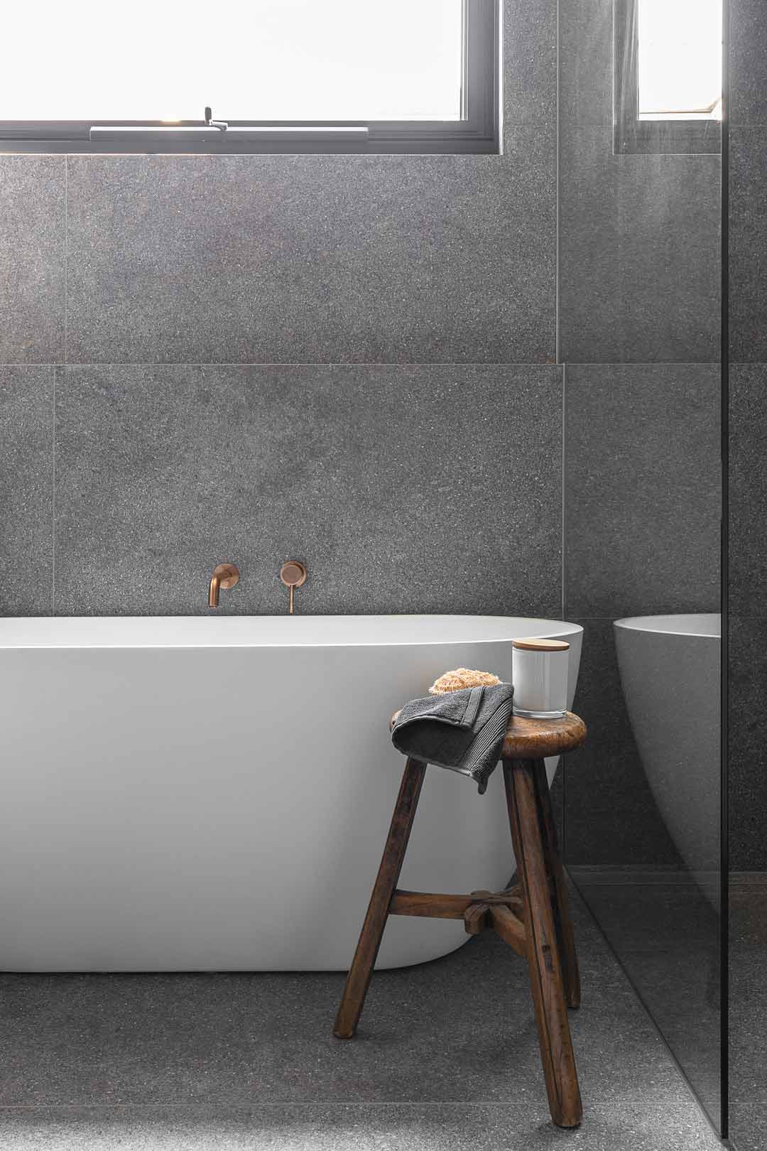 Brushed-copper-tapware-paired-with-a-dark-charcoal-tile-and-a-timber-bath-stool