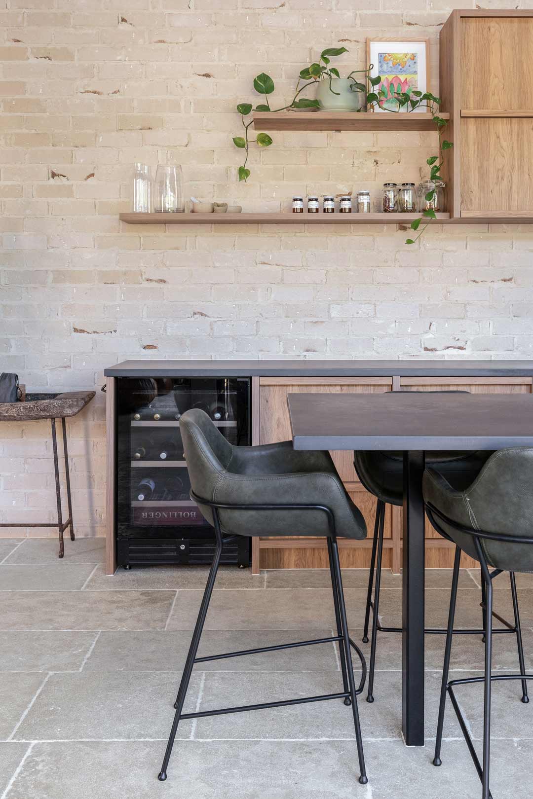 An-open-plan-kitchen-with-green-and-black-bar-stools-a-mini-bar-fridge-and-open-shelving