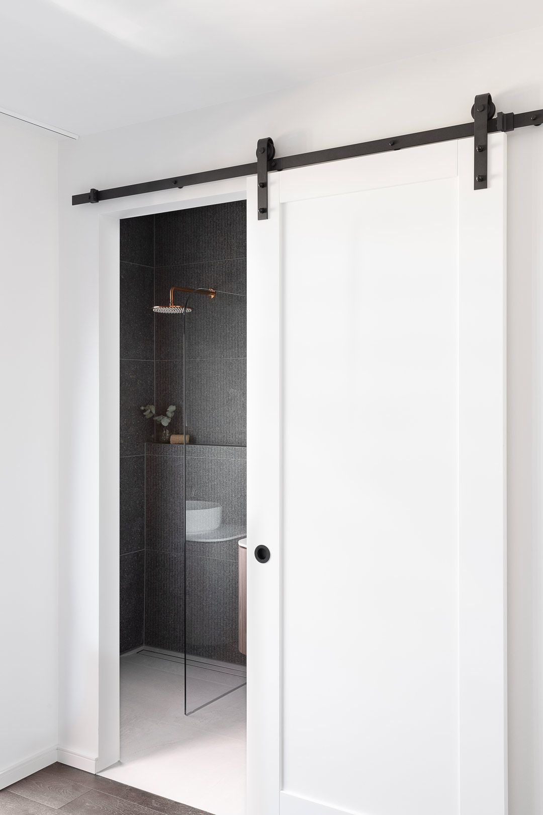 A-sliding-door-into-an-industrial-style-bathroom-with-brushed-copper-shower-fitting-and-dark-grey-tiles