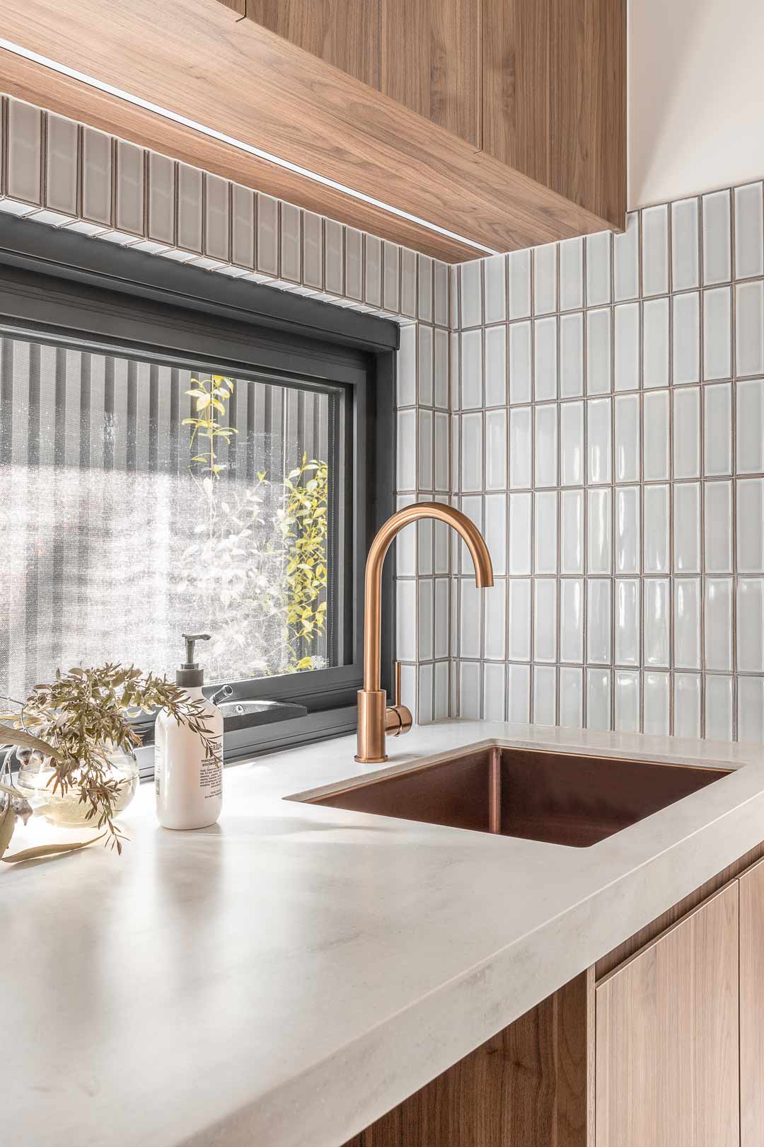 Brushed-copper-mixer-and-sink-in-an-industrial-style-laundry-with-walnut-cabinetry-and-soft-blue-subway-tiles