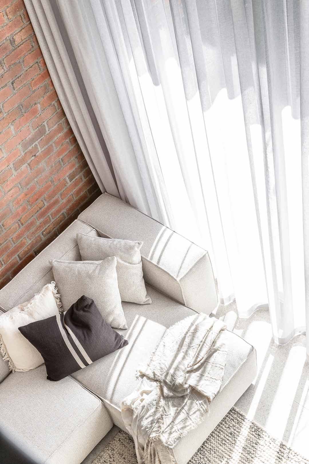Red-bricks-softened-with-a-neutral-toned-couch-and-soft-furnishings-in-an-industrial-style-living-room