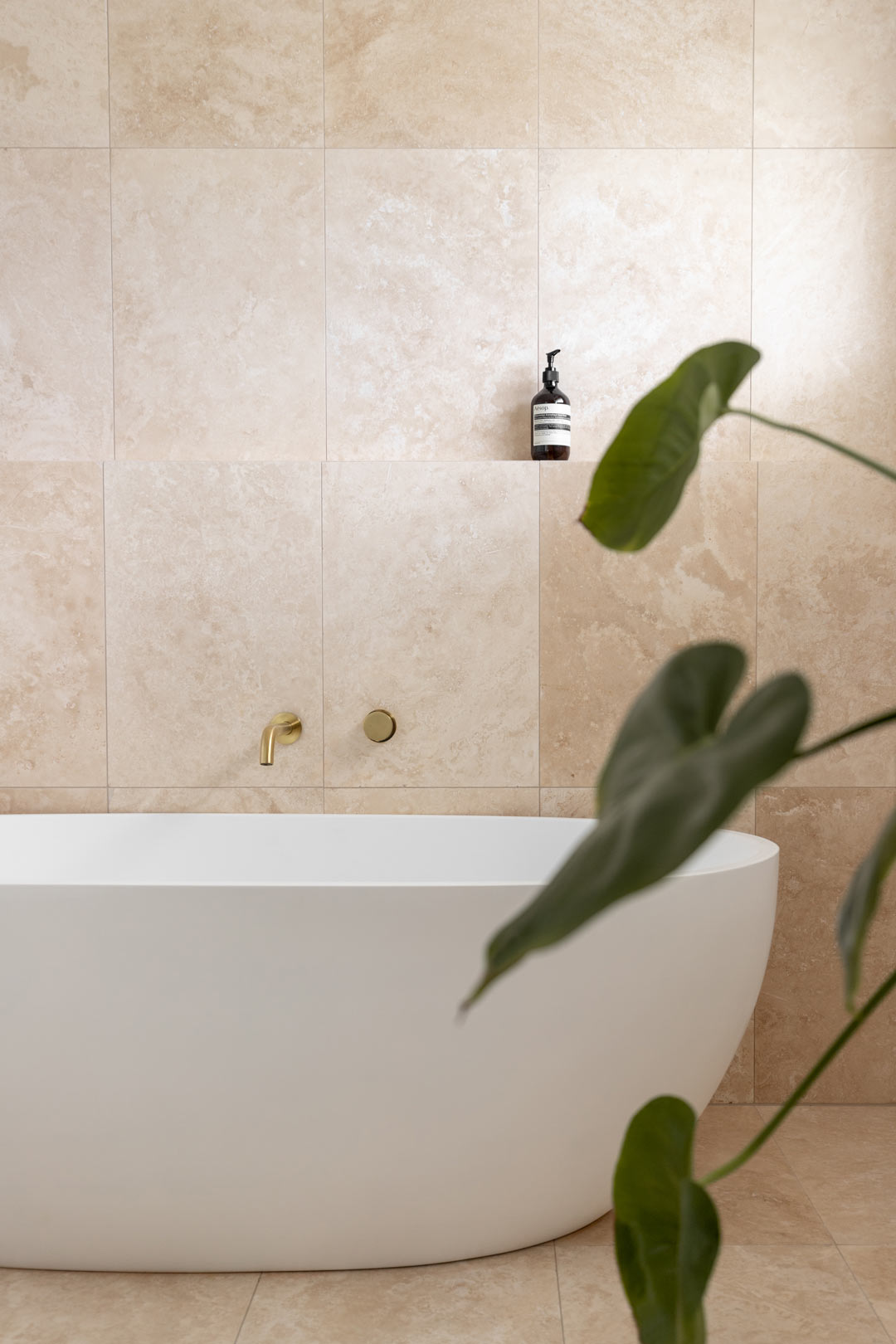 A-calming-bathroom-with-brushed-brass-tapware-and-travertine-tiles-ready-for-relaxation-and-self-care-evening-routine